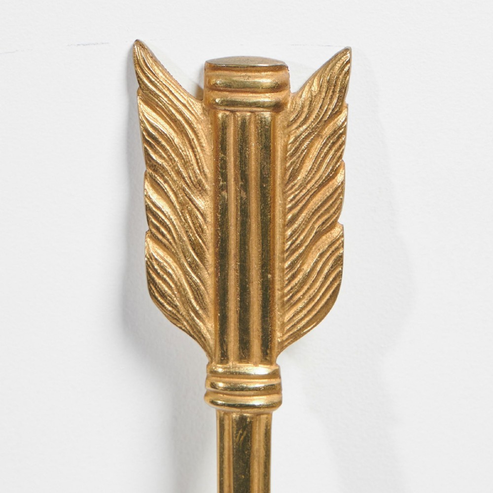 A pair of vertical gilt-metal two-light wall appliques shaped like arrows, featuring central dark octagonal medallions with lion mask reliefs and draped chains. View IV