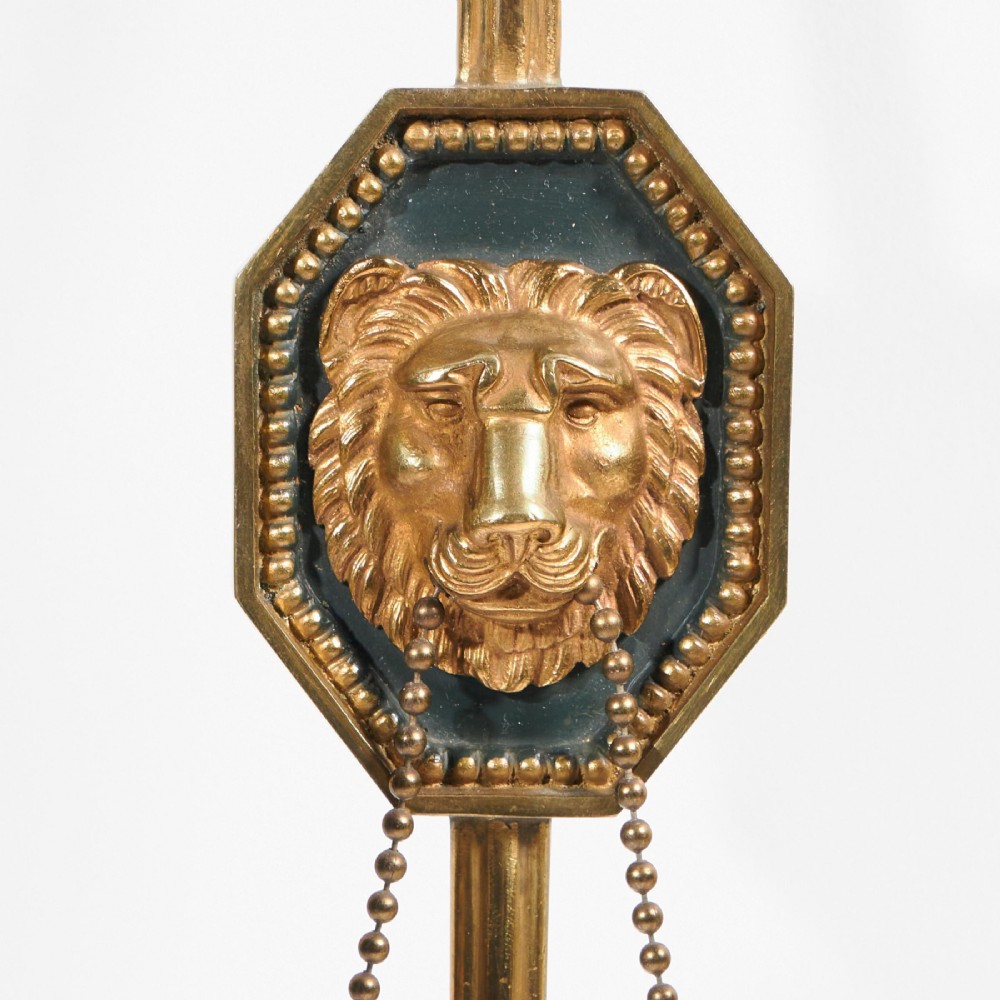 A pair of vertical gilt-metal two-light wall appliques shaped like arrows, featuring central dark octagonal medallions with lion mask reliefs and draped chains. View VII
