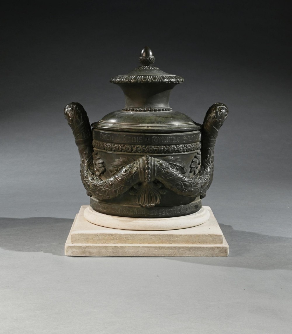 A dark patinated 18th-century Italian bronze vessel featuring relief garlands, handles, and Latin inscriptions, resting on a beige stepped stone plinth. View III