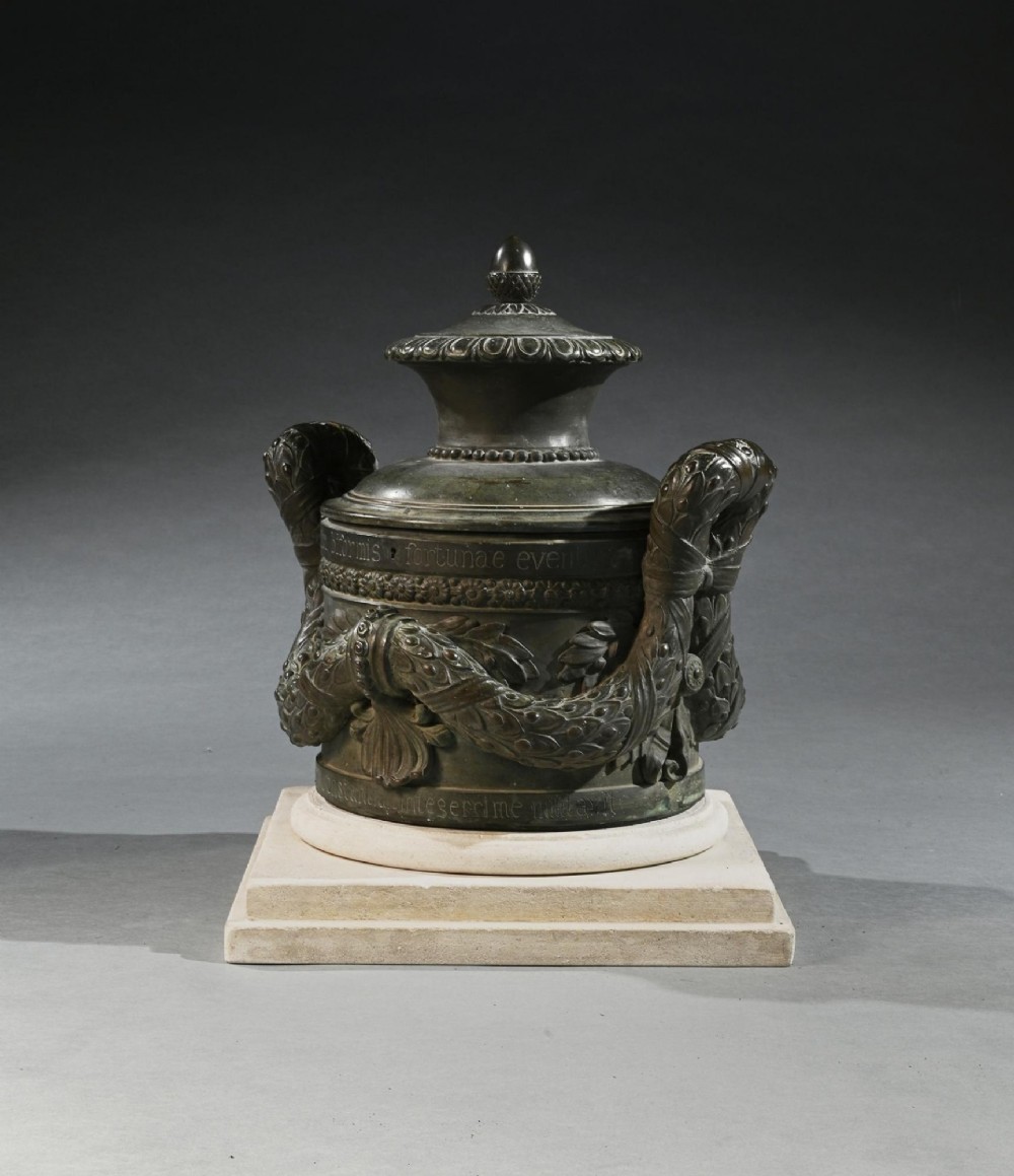 A dark patinated 18th-century Italian bronze vessel featuring relief garlands, handles, and Latin inscriptions, resting on a beige stepped stone plinth. View IV