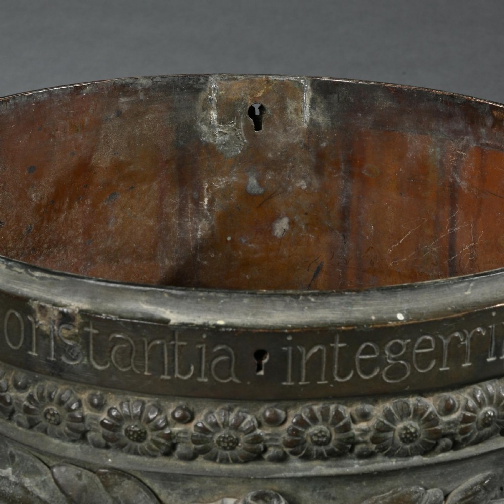 A dark patinated 18th-century Italian bronze vessel featuring relief garlands, handles, and Latin inscriptions, resting on a beige stepped stone plinth. View VIII