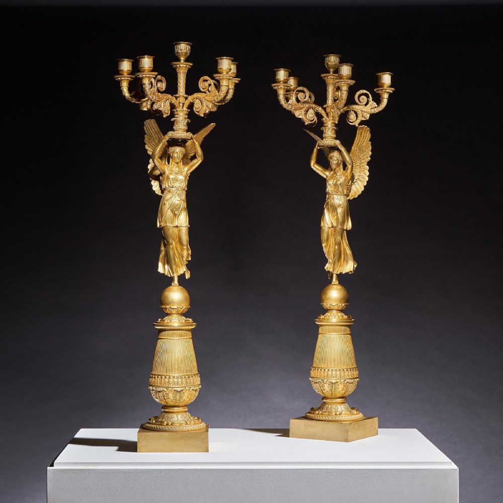 A pair of French Empire gilt bronze candelabra featuring winged Victory figures supporting multi-arm candle holders on pedestals.