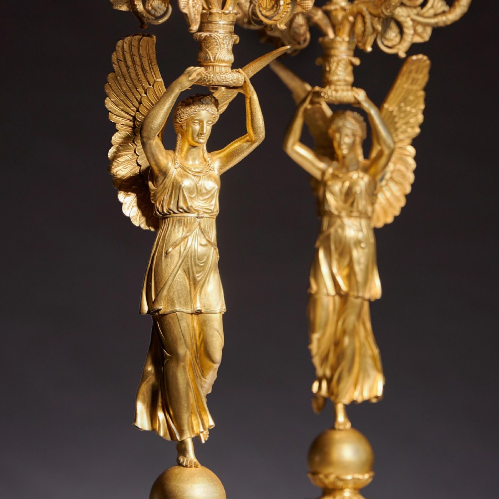 A pair of French Empire gilt bronze candelabra featuring winged Victory figures supporting multi-arm candle holders on pedestals. View V