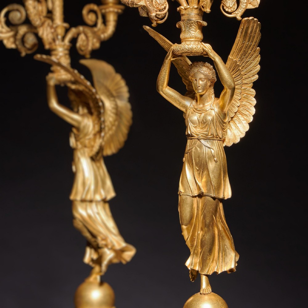 A pair of French Empire gilt bronze candelabra featuring winged Victory figures supporting multi-arm candle holders on pedestals. View VII