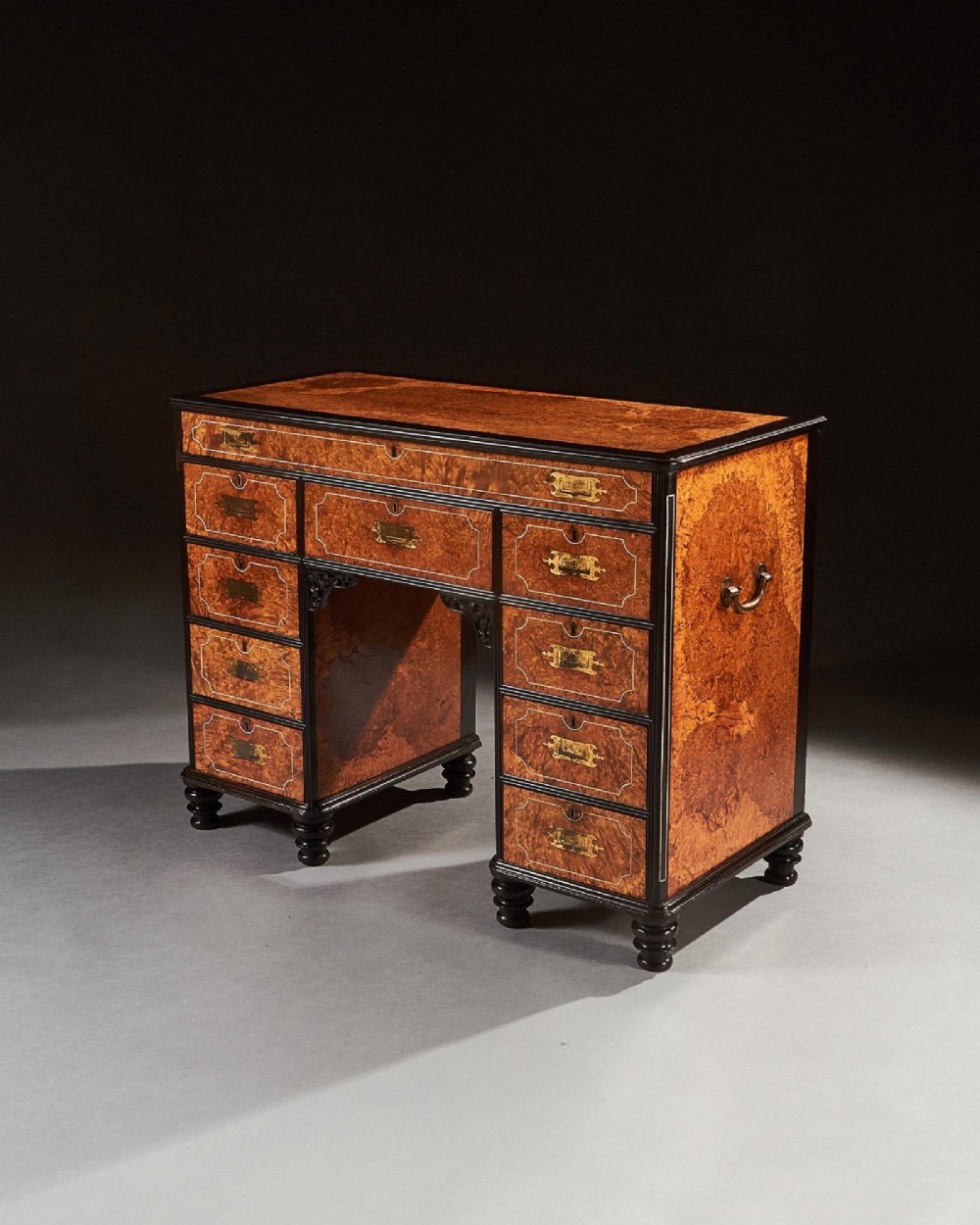 A 19th-century Chinese export kneehole campaign desk crafted from figured amboyna wood with ebony borders and brass carrying handles. View V