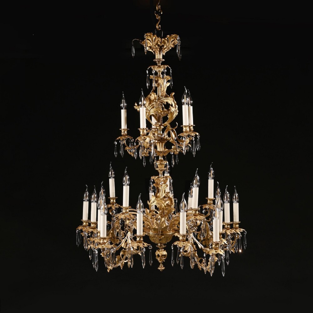 A late nineteenth-century Louis XV style gilt bronze chandelier with twenty-five candle lights across two tiers, embellished with cut glass droplets and ornate scrolling metalwork.