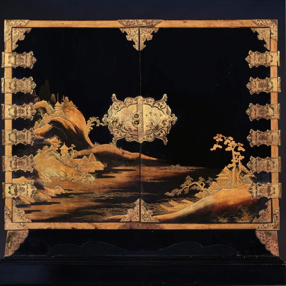 A black lacquered Japanese cabinet decorated with gold maki-e landscape scenes, featuring ornate brass mounts and elevated on a simple black stand. View II