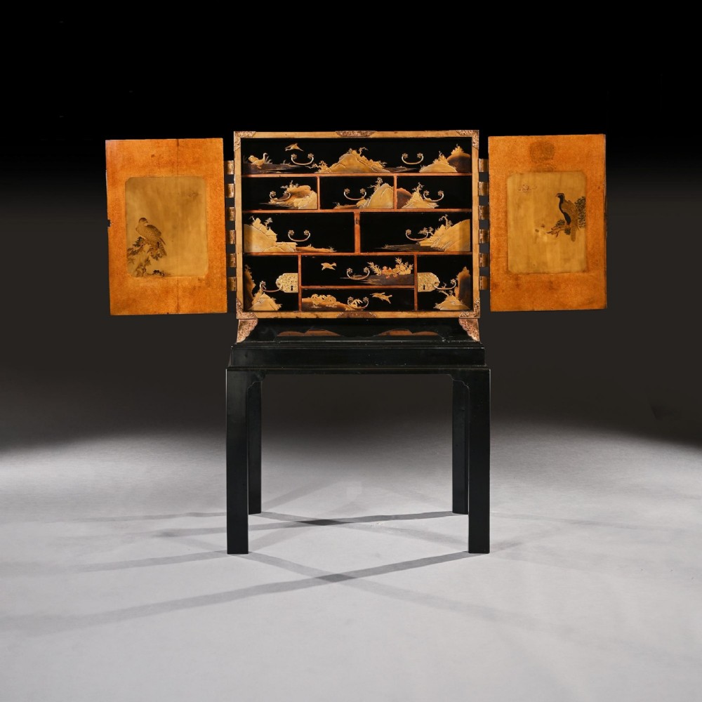 A black lacquered Japanese cabinet decorated with gold maki-e landscape scenes, featuring ornate brass mounts and elevated on a simple black stand. View III