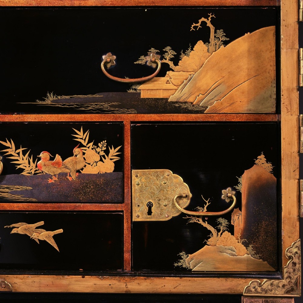 A black lacquered Japanese cabinet decorated with gold maki-e landscape scenes, featuring ornate brass mounts and elevated on a simple black stand. View VI