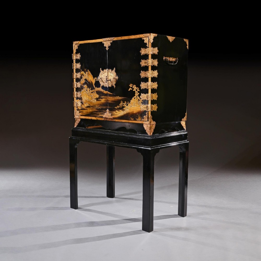 A black lacquered Japanese cabinet decorated with gold maki-e landscape scenes, featuring ornate brass mounts and elevated on a simple black stand. View VII