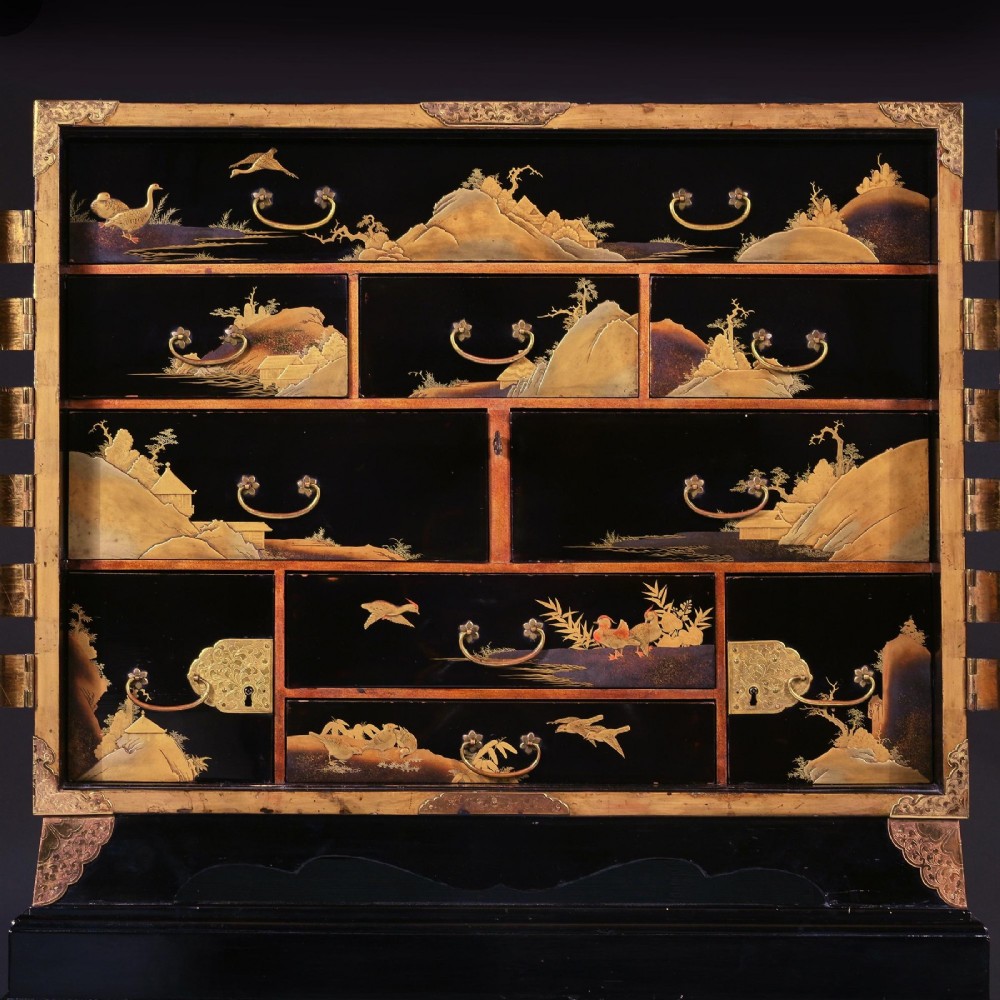 A black lacquered Japanese cabinet decorated with gold maki-e landscape scenes, featuring ornate brass mounts and elevated on a simple black stand. View VIII