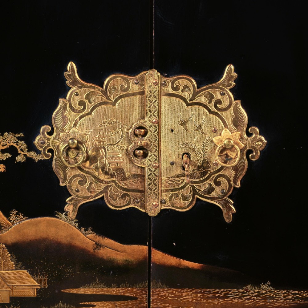 A black lacquered Japanese cabinet decorated with gold maki-e landscape scenes, featuring ornate brass mounts and elevated on a simple black stand. View XII