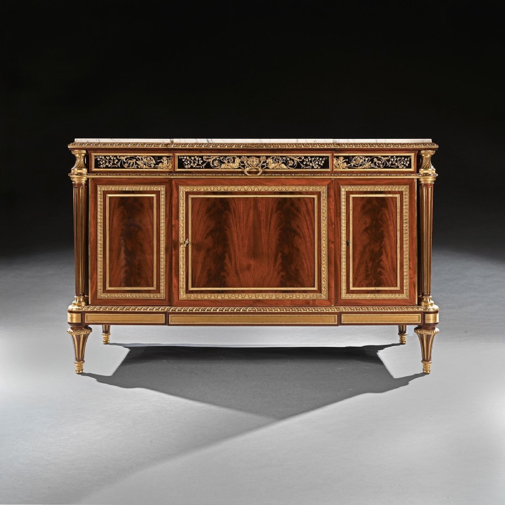 A 19th-century French Louis XVI style flame mahogany commode featuring ornate gilt-bronze mounts, three paneled cupboard doors, fluted legs, and a white marble top.