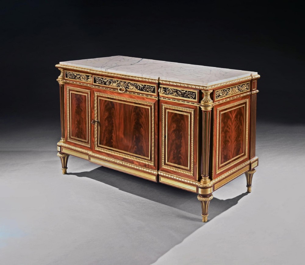 A 19th-century French Louis XVI style flame mahogany commode featuring ornate gilt-bronze mounts, three paneled cupboard doors, fluted legs, and a white marble top. View III