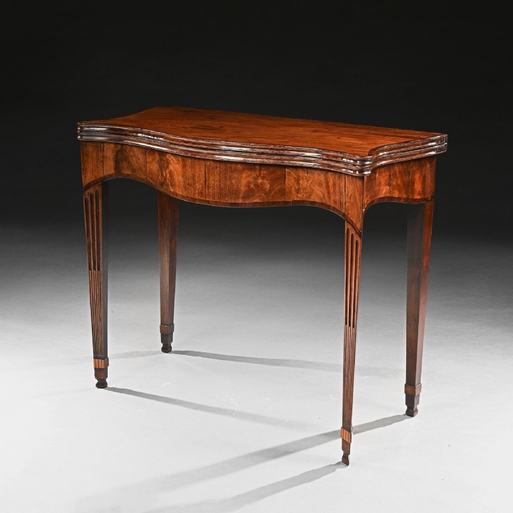 A George III mahogany tea table featuring a serpentine fold-over top, fluted tapered legs, and flame mahogany veneers on the frieze.