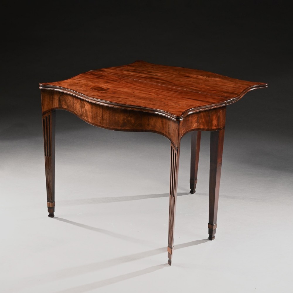 A George III mahogany tea table featuring a serpentine fold-over top, fluted tapered legs, and flame mahogany veneers on the frieze. View IV