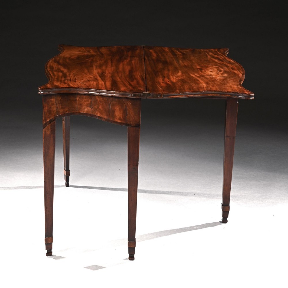 A George III mahogany tea table featuring a serpentine fold-over top, fluted tapered legs, and flame mahogany veneers on the frieze. View V