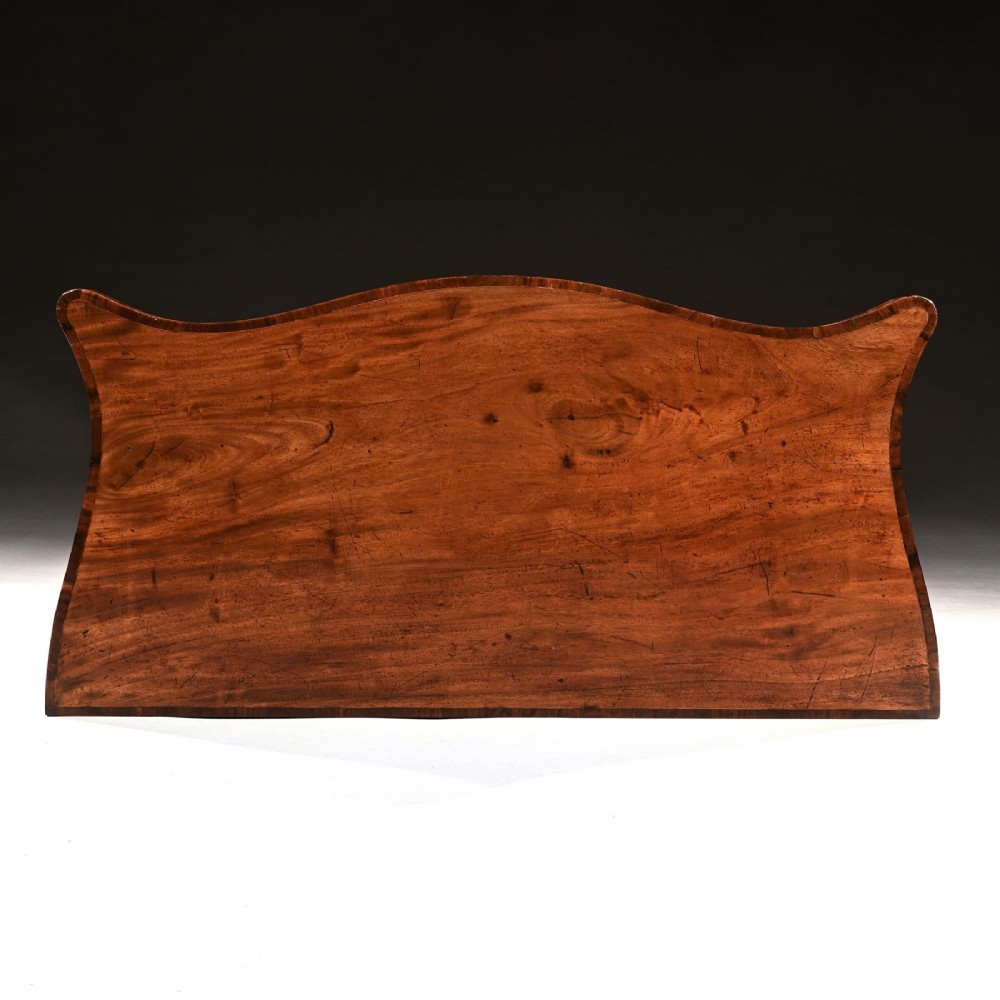 A George III mahogany tea table featuring a serpentine fold-over top, fluted tapered legs, and flame mahogany veneers on the frieze. View VII
