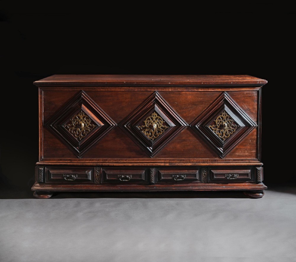 A dark mahogany Portuguese colonial chest featuring three raised diamond-moulded panels with central pierced brass mounts above a row of lower drawers. View II