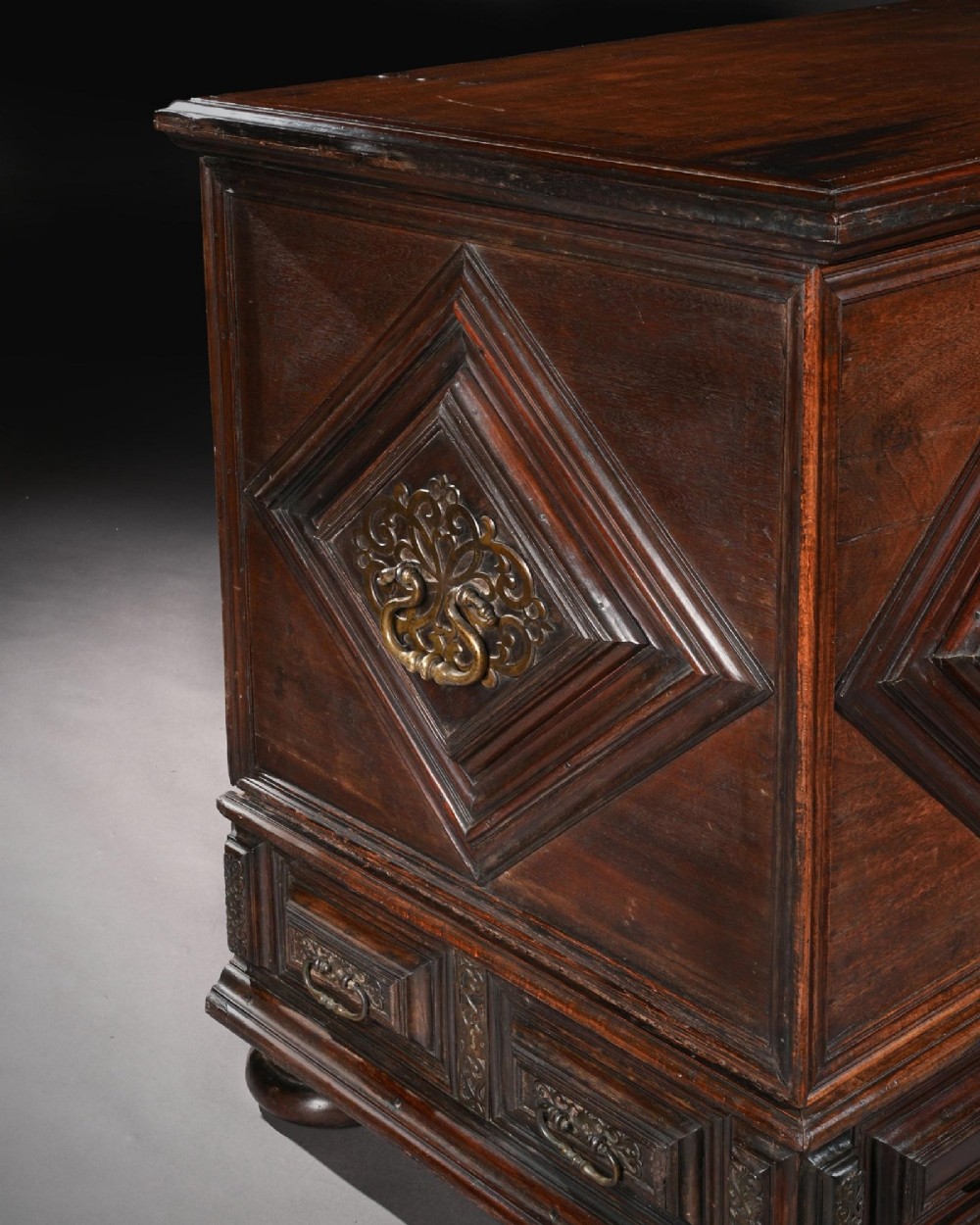 A dark mahogany Portuguese colonial chest featuring three raised diamond-moulded panels with central pierced brass mounts above a row of lower drawers. View VII