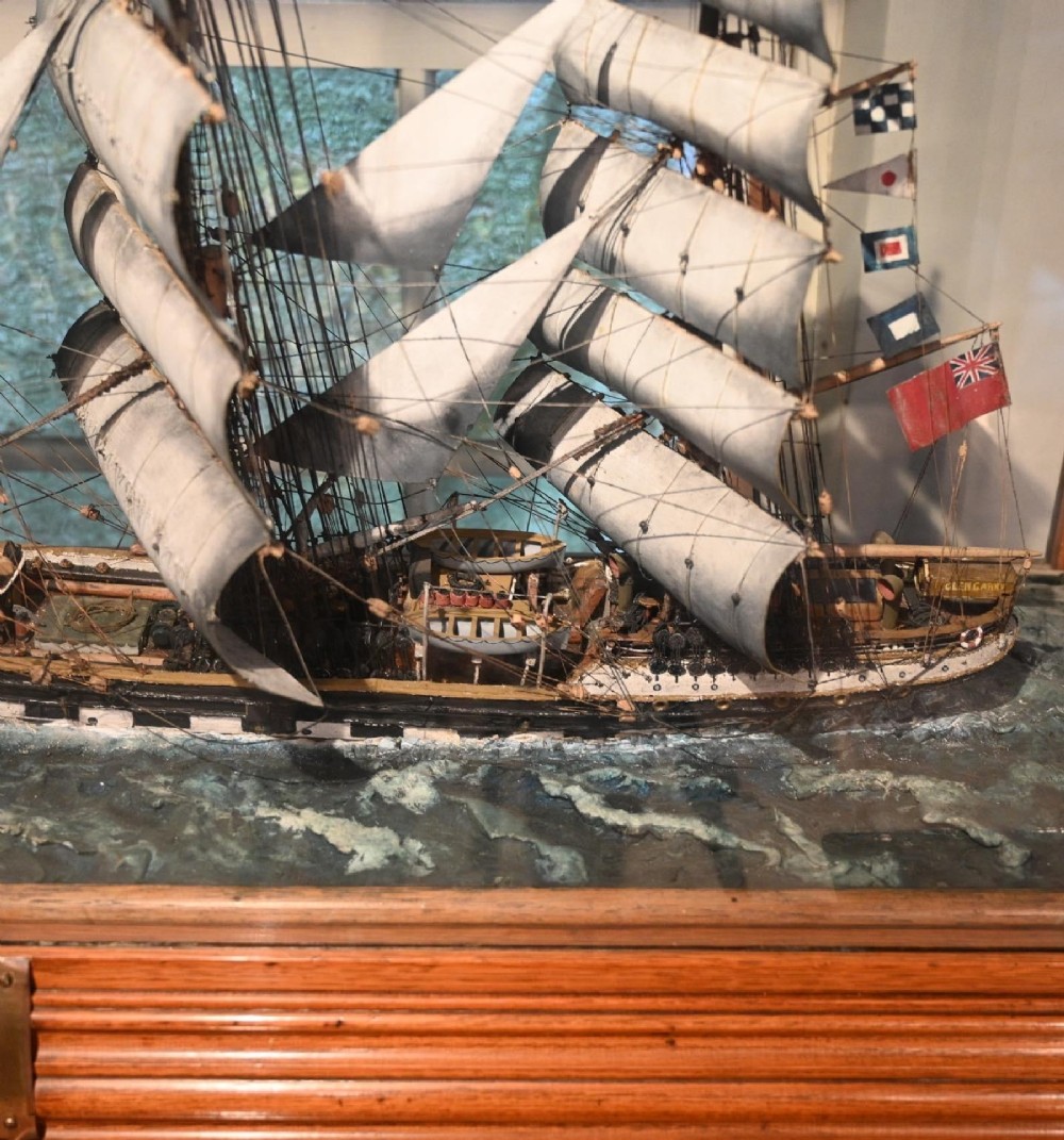 A detailed scale model of a three-masted tea clipper ship in full sail set within a seascaped display inside a glazed oak wood case with a brass plaque. View V