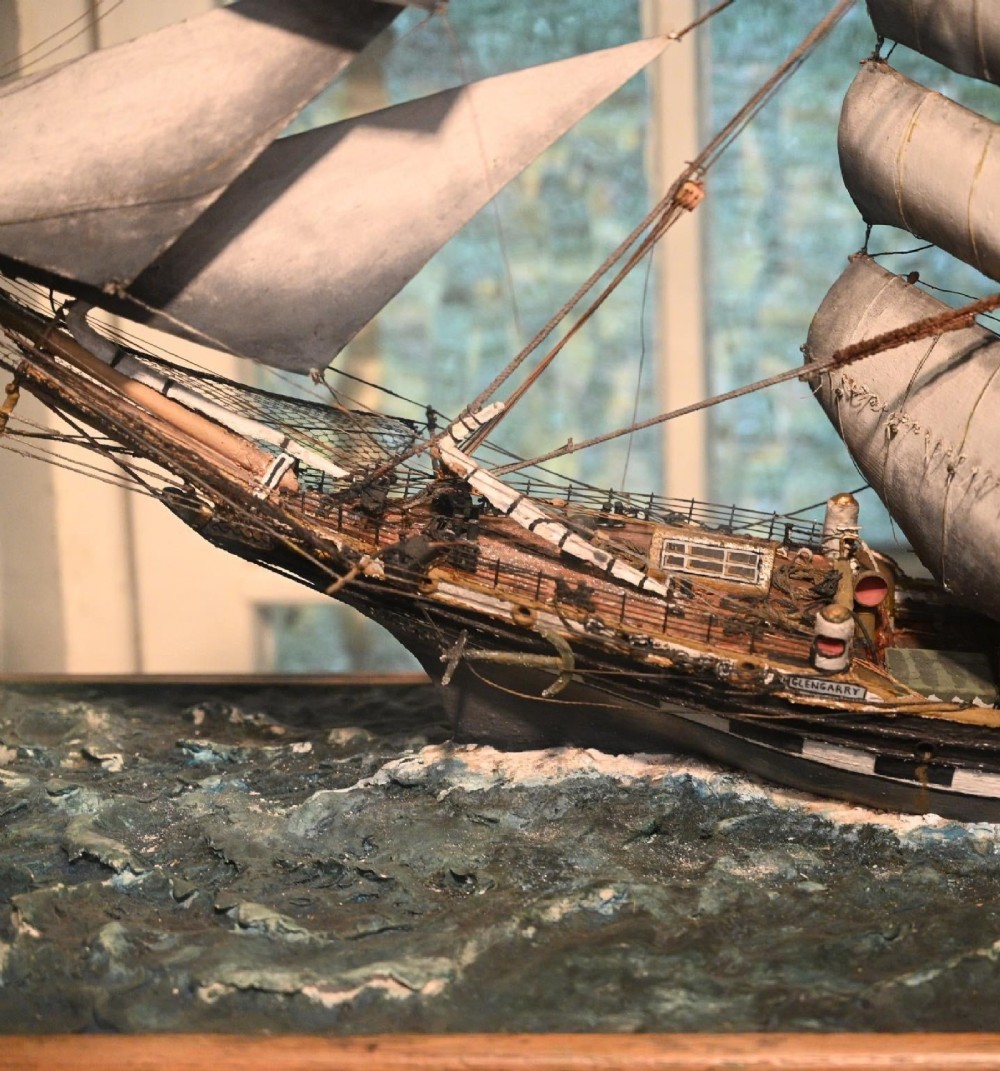 A detailed scale model of a three-masted tea clipper ship in full sail set within a seascaped display inside a glazed oak wood case with a brass plaque. View VII