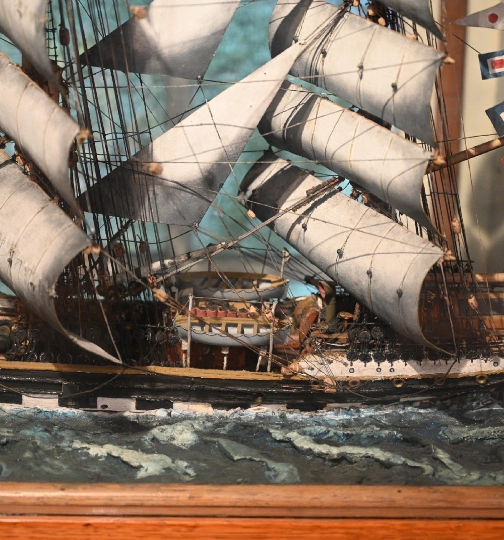A detailed scale model of a three-masted tea clipper ship in full sail set within a seascaped display inside a glazed oak wood case with a brass plaque. View VIII