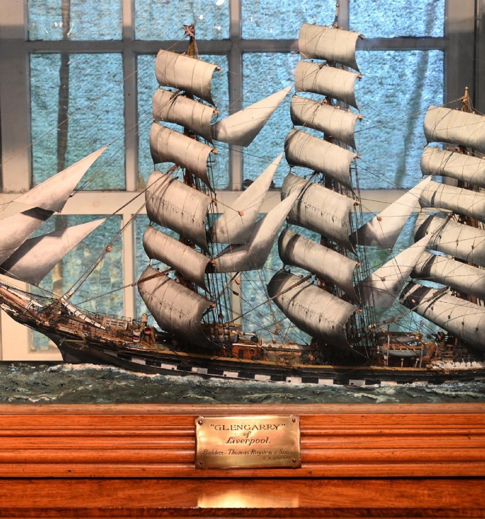 A detailed scale model of a three-masted tea clipper ship in full sail set within a seascaped display inside a glazed oak wood case with a brass plaque. View IX