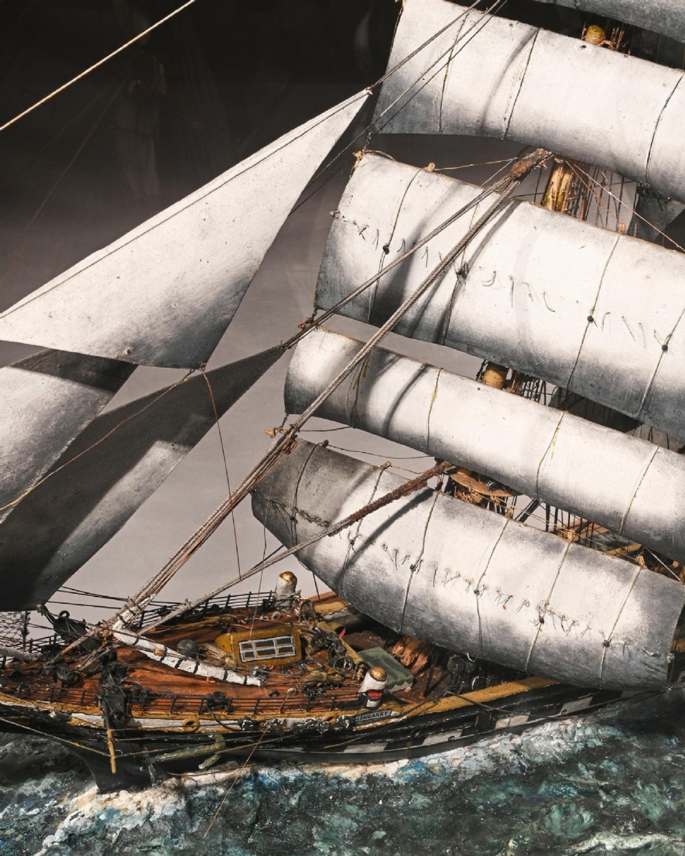 A detailed scale model of a three-masted tea clipper ship in full sail set within a seascaped display inside a glazed oak wood case with a brass plaque. View XI