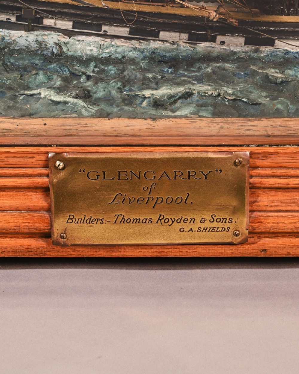 A detailed scale model of a three-masted tea clipper ship in full sail set within a seascaped display inside a glazed oak wood case with a brass plaque. View XIV