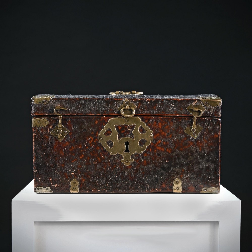 A 17th-century dark brown leather-bound travelling box with ornate pierced brass corner mounts, side latches, central lock plate, and a top carrying handle. View II