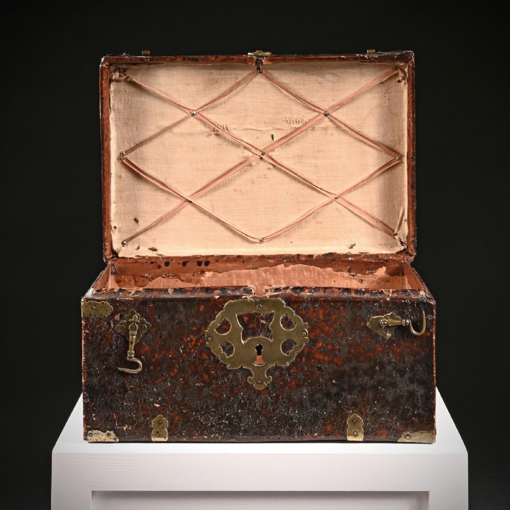 A 17th-century dark brown leather-bound travelling box with ornate pierced brass corner mounts, side latches, central lock plate, and a top carrying handle. View V