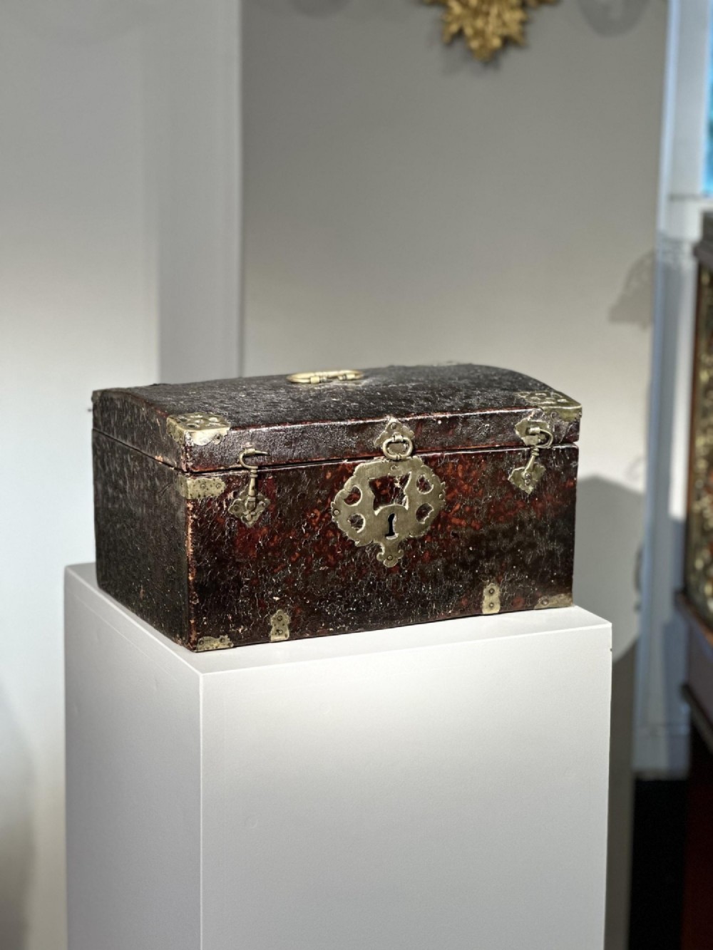 A 17th-century dark brown leather-bound travelling box with ornate pierced brass corner mounts, side latches, central lock plate, and a top carrying handle. View VII