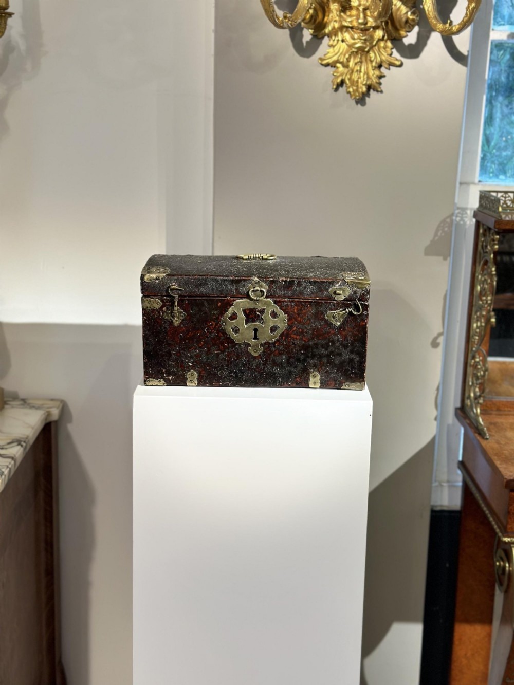 A 17th-century dark brown leather-bound travelling box with ornate pierced brass corner mounts, side latches, central lock plate, and a top carrying handle. View VIII