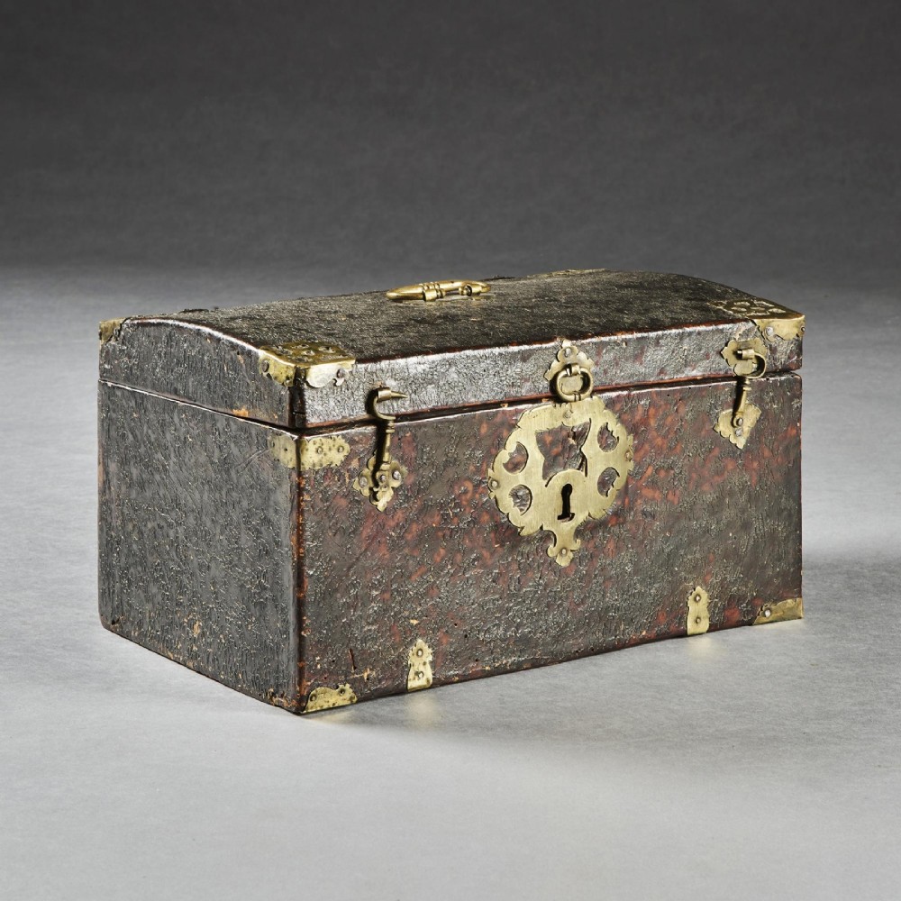 A 17th-century dark brown leather-bound travelling box with ornate pierced brass corner mounts, side latches, central lock plate, and a top carrying handle. View IX