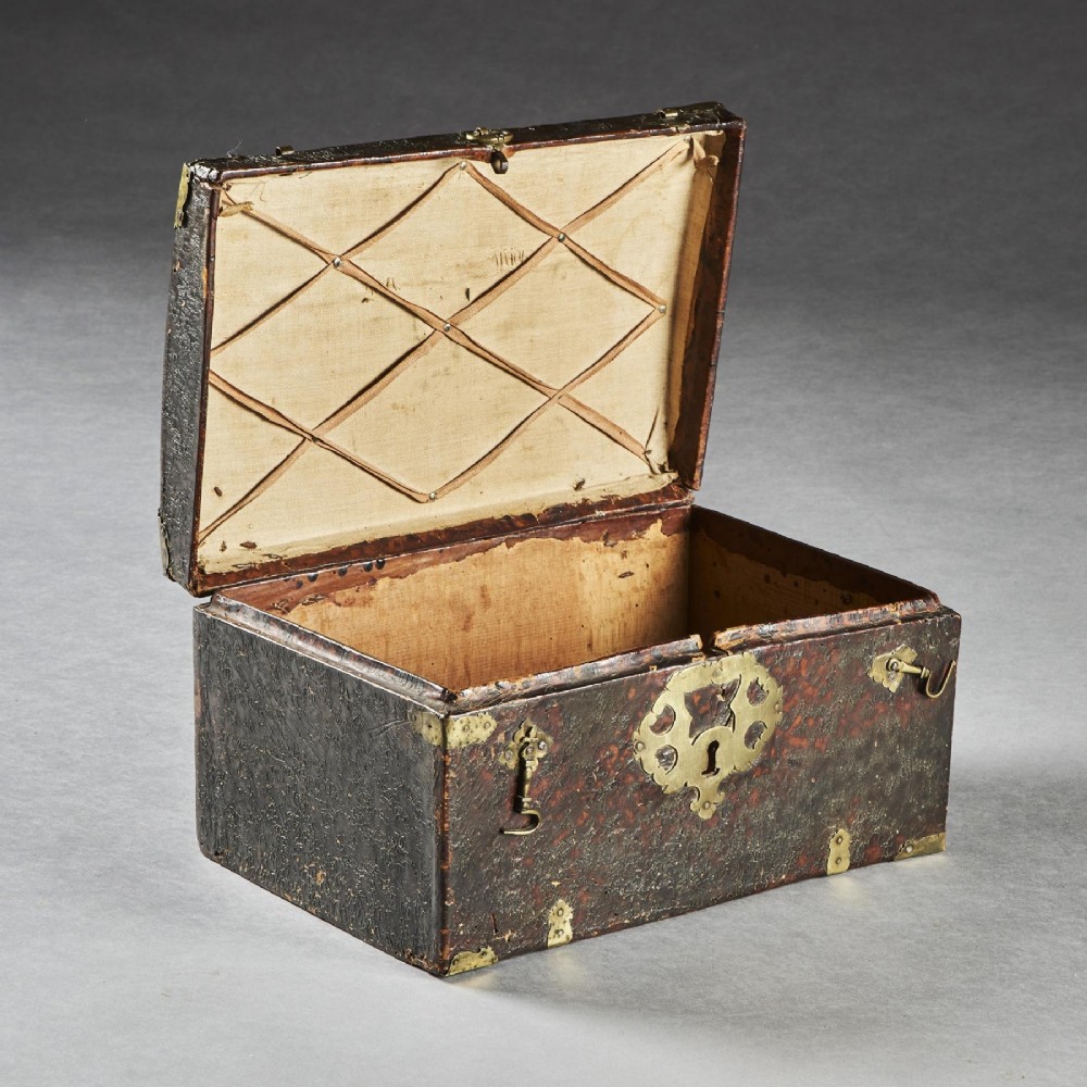 A 17th-century dark brown leather-bound travelling box with ornate pierced brass corner mounts, side latches, central lock plate, and a top carrying handle. View X