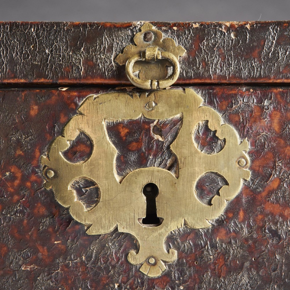 A 17th-century dark brown leather-bound travelling box with ornate pierced brass corner mounts, side latches, central lock plate, and a top carrying handle. View XI