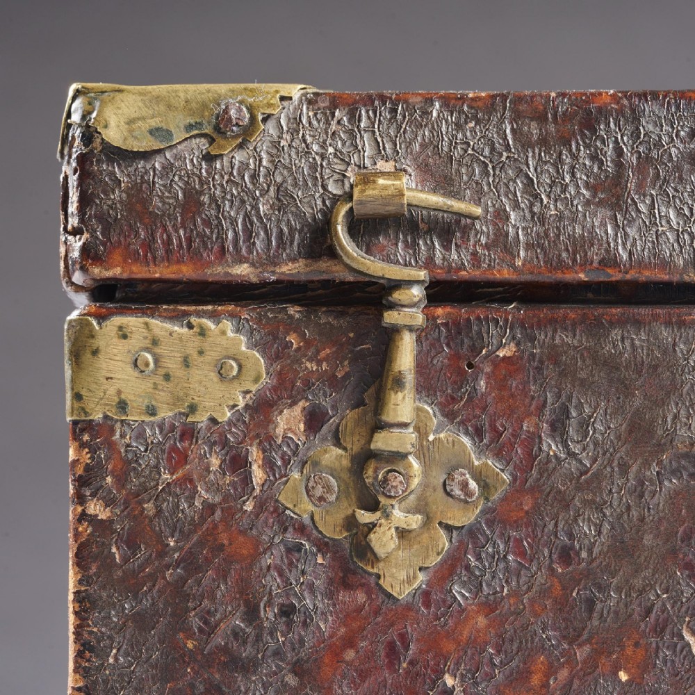 A 17th-century dark brown leather-bound travelling box with ornate pierced brass corner mounts, side latches, central lock plate, and a top carrying handle. View XII
