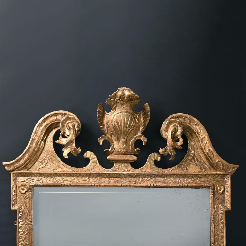 An 18th-century George II carved gesso and giltwood wall mirror featuring a broken arch pediment with a central shell motif and foxed glass plate. View II