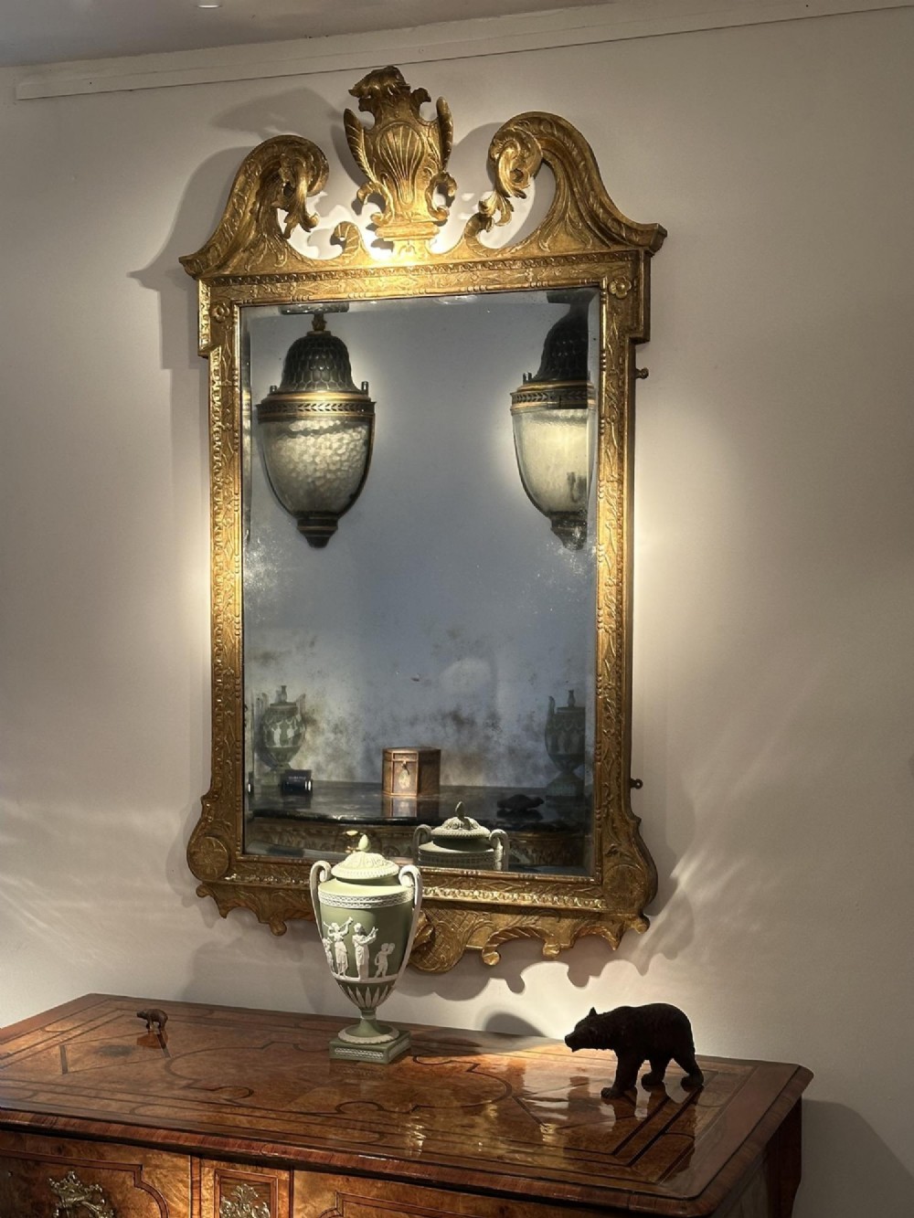 An 18th-century George II carved gesso and giltwood wall mirror featuring a broken arch pediment with a central shell motif and foxed glass plate. View V