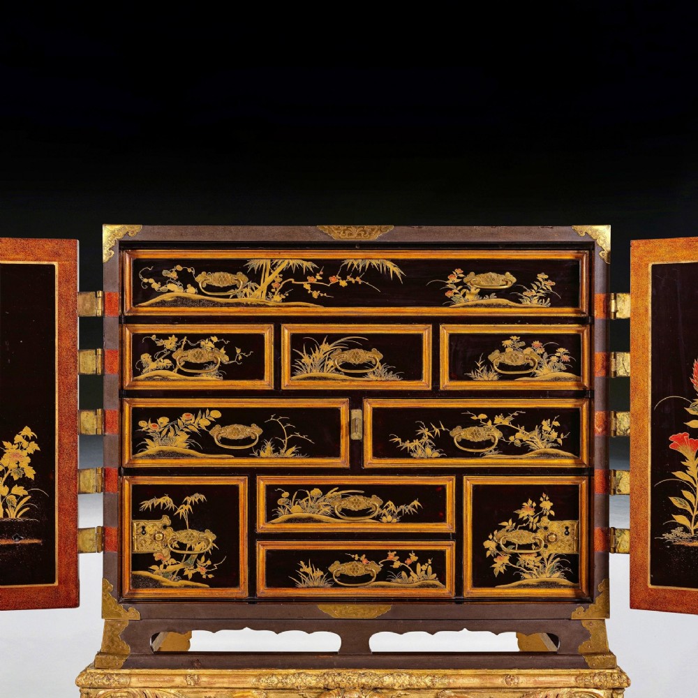 A black Japanese urushi lacquer cabinet decorated with gold landscape scenes and metal corner mounts, supported on a carved French Regence giltwood stand with cabriole legs. View V
