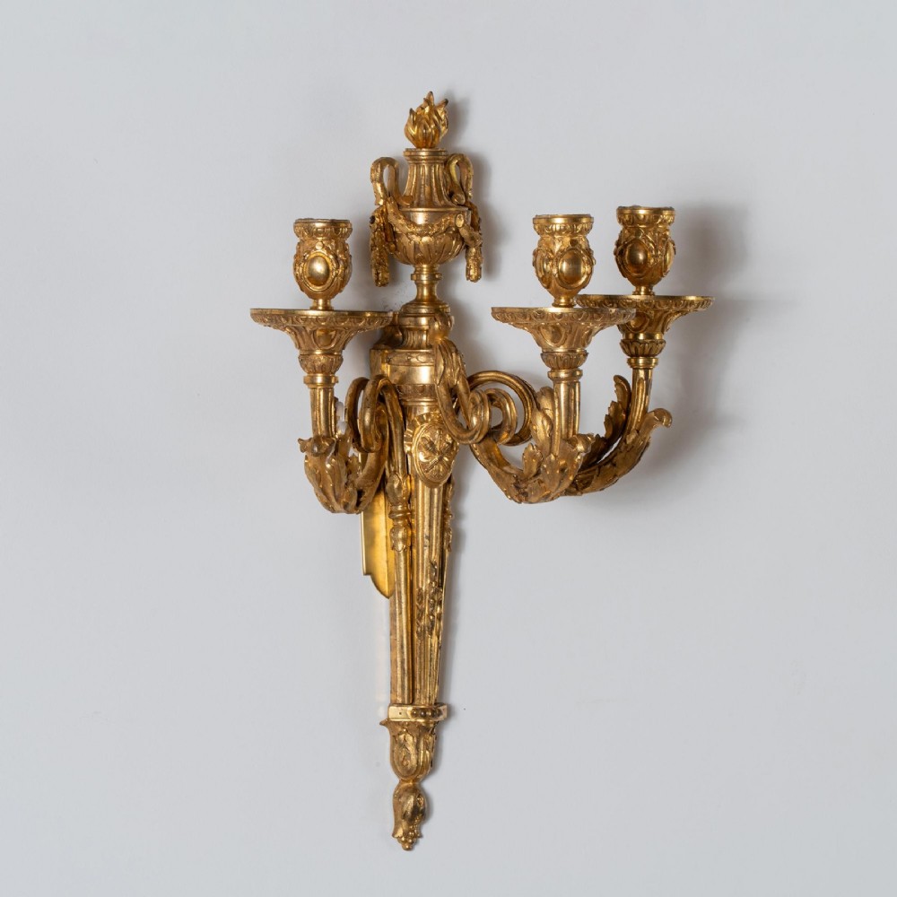 A set of four French Louis XV style gilded bronze wall lights, each featuring three scrolling foliate arms supporting candle sockets and an urn finial backplate. View V
