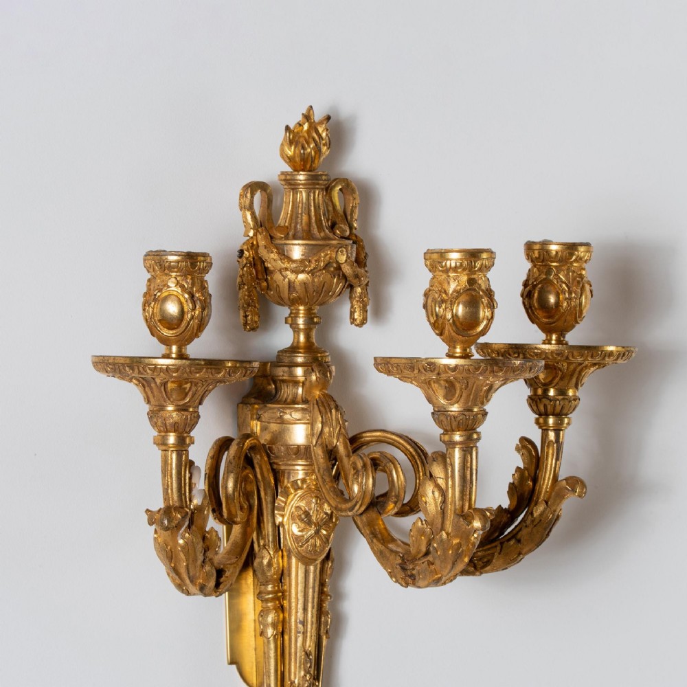 A set of four French Louis XV style gilded bronze wall lights, each featuring three scrolling foliate arms supporting candle sockets and an urn finial backplate. View VI