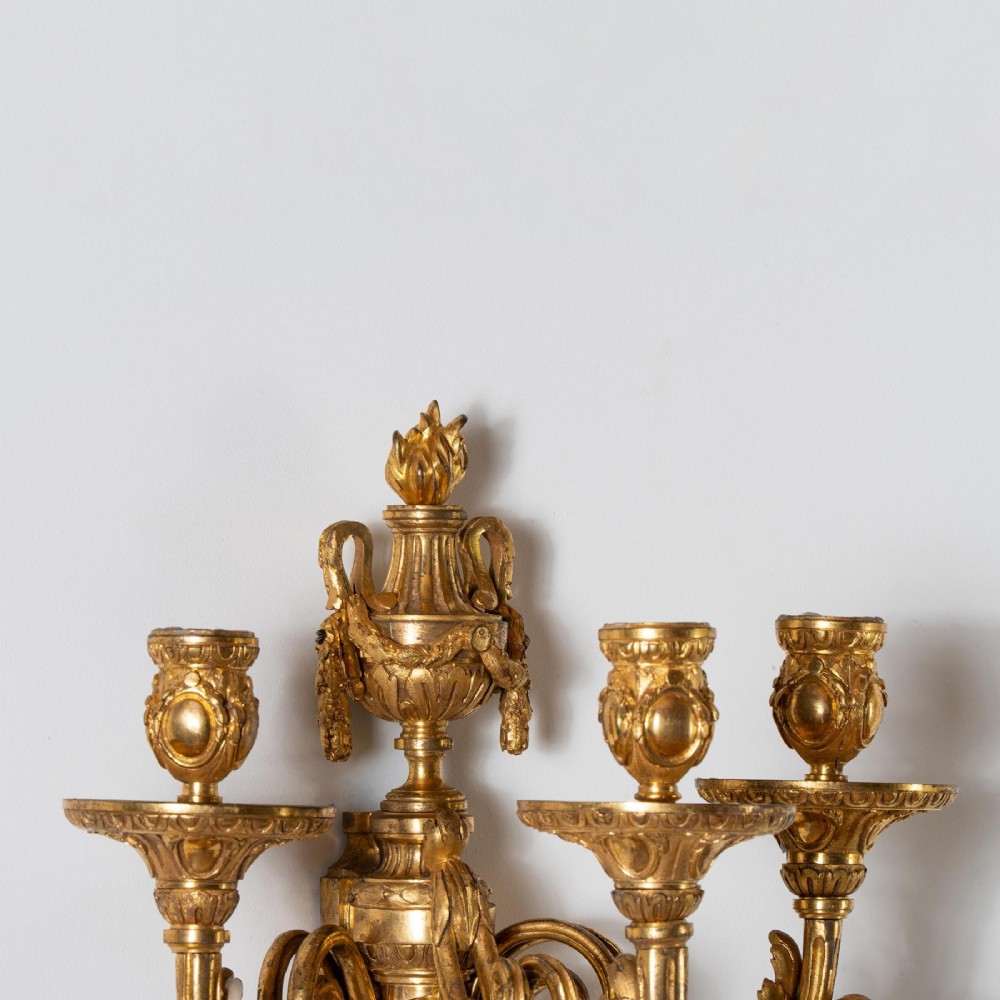 A set of four French Louis XV style gilded bronze wall lights, each featuring three scrolling foliate arms supporting candle sockets and an urn finial backplate. View VII
