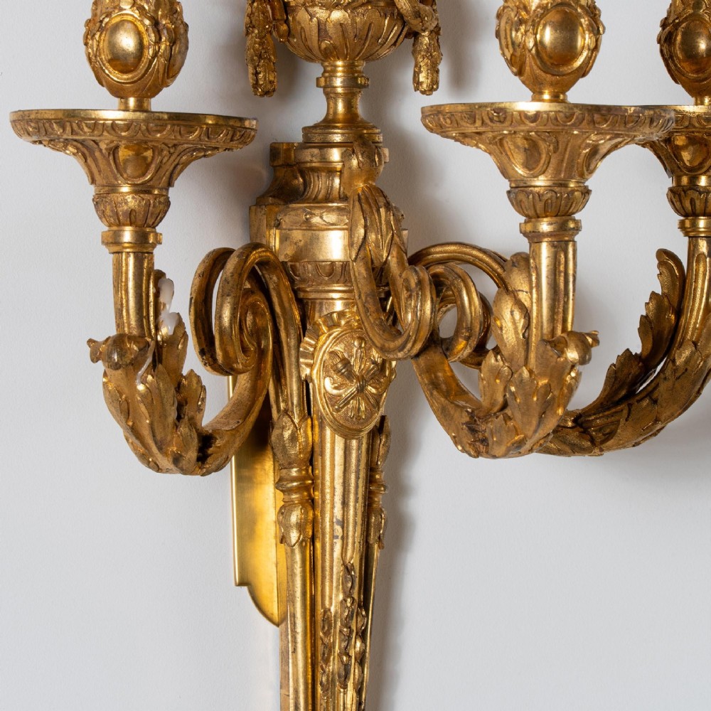 A set of four French Louis XV style gilded bronze wall lights, each featuring three scrolling foliate arms supporting candle sockets and an urn finial backplate. View VIII