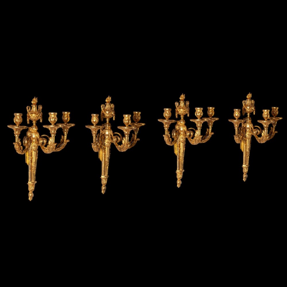 A set of four French Louis XV style gilded bronze wall lights, each featuring three scrolling foliate arms supporting candle sockets and an urn finial backplate. View XII
