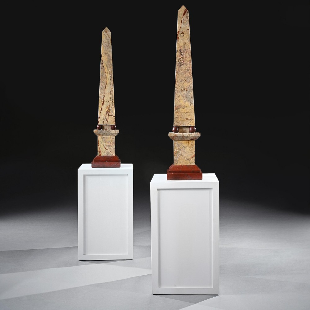 A pair of tall, veined marble obelisks carved from Portasanta and Rosso Antico marble with polished spherical details on tiered square bases.