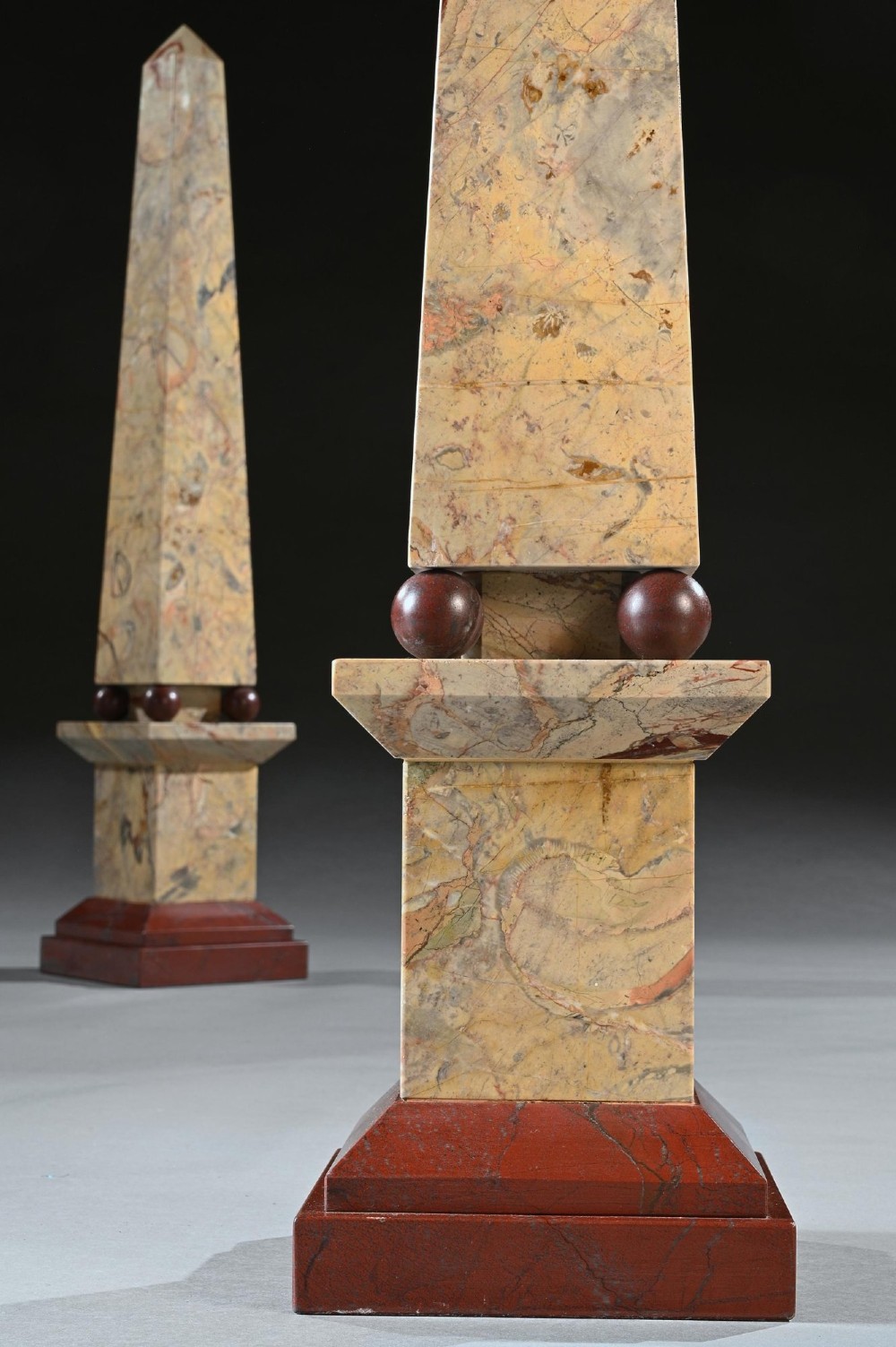 A pair of tall, veined marble obelisks carved from Portasanta and Rosso Antico marble with polished spherical details on tiered square bases. View VI
