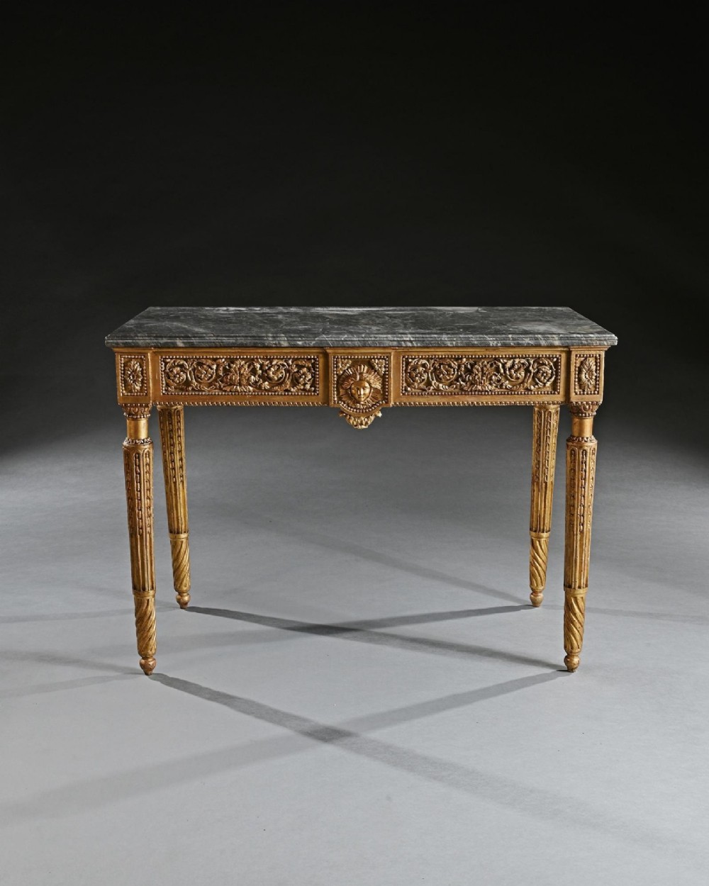 An 18th-century Italian Neoclassical console table featuring a grey veined marble top, an intricate giltwood frieze with a central carved mask, and fluted legs. View II