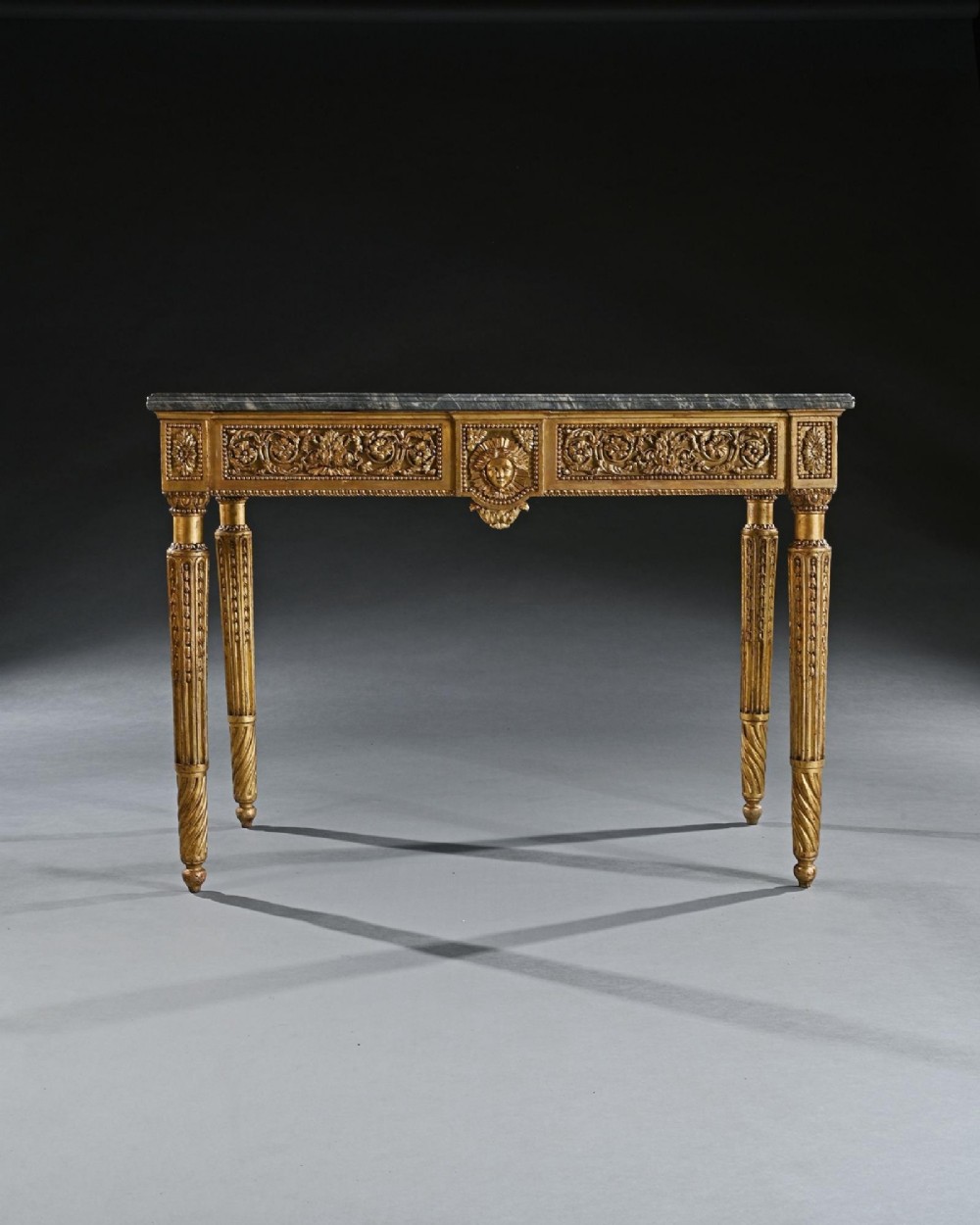 An 18th-century Italian Neoclassical console table featuring a grey veined marble top, an intricate giltwood frieze with a central carved mask, and fluted legs. View IV